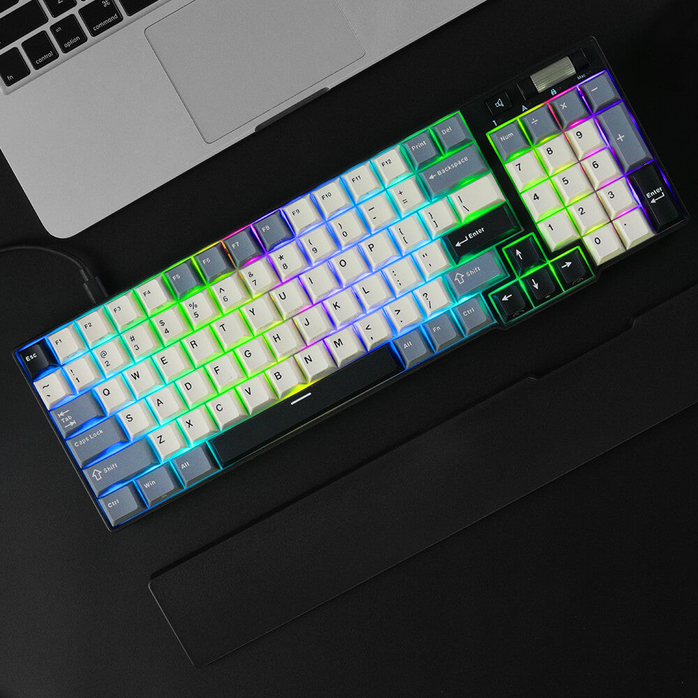 Mechanical keyboard with RGB lighting on a dark surface next to a laptop.